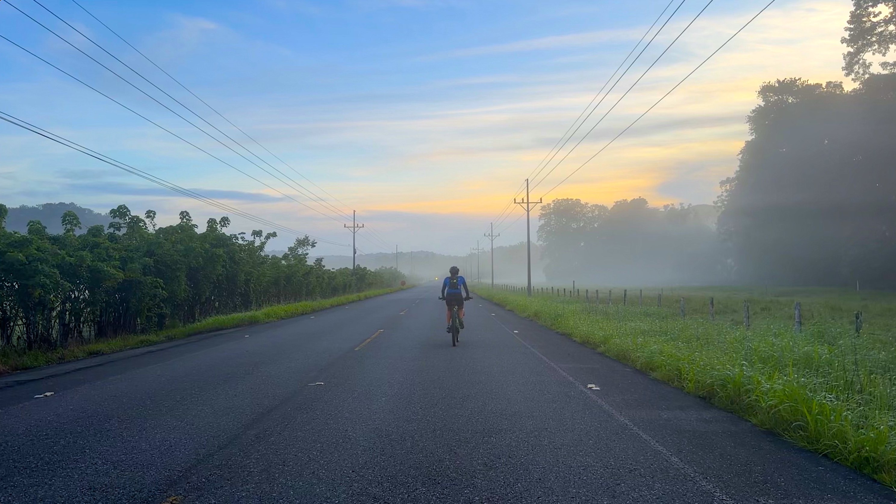 Ciclista de espaldas en una carretera de Costa Rica con la niebla del amanecer